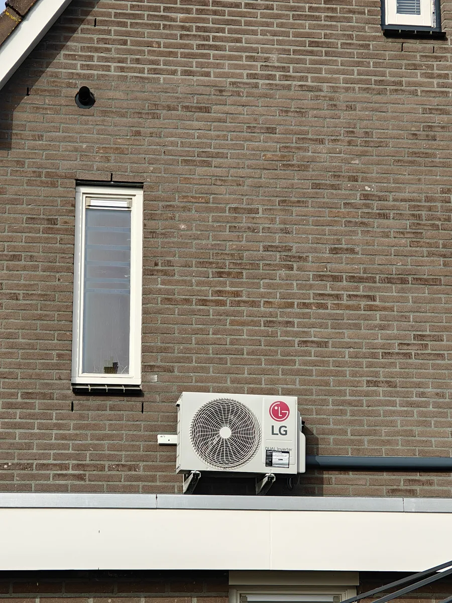 Witte leidinggoten van de airco langs de gemetselde buitengevel